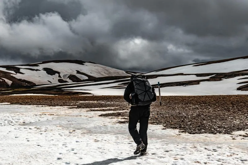 A lone hiker crosses a snowy mountain pass beneath dark storm clouds.